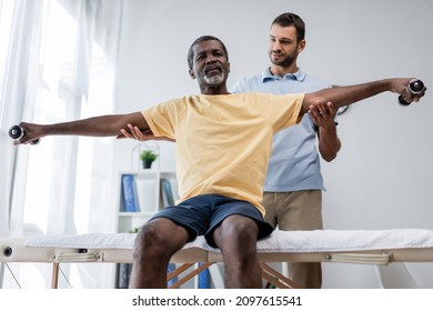 physical therapist supporting mature african american man training with dumbbells