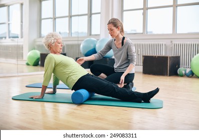 Physical therapist working with active senior woman at rehab.  Old woman exercising using foam roller with personal trainer at gym. - Powered by Shutterstock