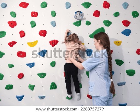 Physical therapist working with little girl in climbing wall. sensory integration room. Physiotherapy and neuro corrections in children therapy center