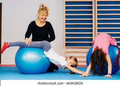 Physical Therapist Working With Little Girls In School Gymnasium, Exercising With Fitness Ball