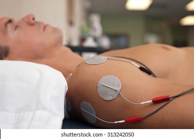 Physical therapy or chiropractic treatment of a male patient's injured shoulder using transcutaneous interferential electrical stimulation (TENS) for pain management.