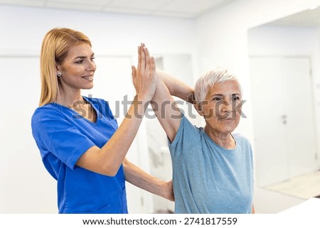 Physical therapy session for senior. Elderly woman with arm problem, Healthcare And Medicine concept. Professional physiotherapist in blue uniform helping patient with shoulder stretching exercise.