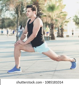 Physically fit glad man doing stretching exercises on morning beach