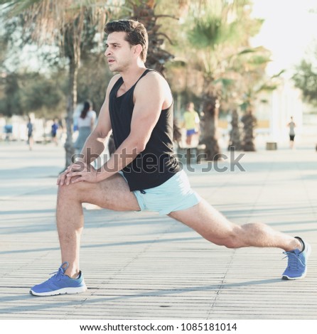 Physically fit glad man doing stretching exercises on morning beach