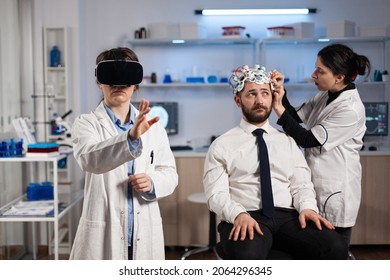 Physician doctor with virtual reality headset while neurologist woman adjusting eeg scanner of man patient analyzing brain evolution during neurology experiment. Scientist engineer using high tech