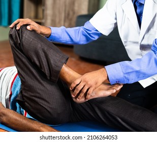 Physician exercising old man to stretch legs at home for joint pain relief - concept of senior people home health check, knee joint pain treatment and medical treatment or therapy