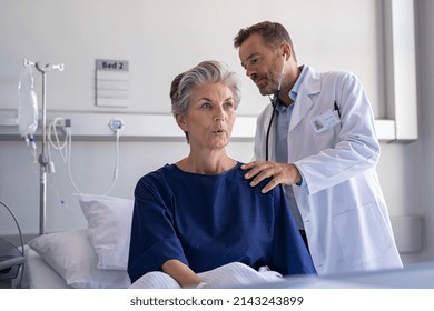 Physician listening senior woman back lungs through stethoscope. Hospitalized elderly woman sitting on bed while doctor checking her breathe and heartbeat. Doctor auscultate heart of old patient. - Shutterstock ID 2143243899