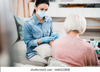 Physician In Medical Face Mask Holding Syringe While Senior Lady Keeping Arm On Cushion Stock Photo