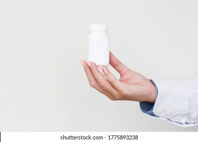 Physician Medicine Doctor Or Pharmacist Sitting At Worktable, Holding Or Showing Bottle Of Pills In Hand And Writing Prescription On Special Form. Medical Care, Pharmacy Or Health Insurance Concept