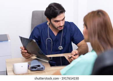 Physician Men Talking And Looking At X Ray Film With Woman Patient At Clinic. Doctor Discussing With Patient In Medical Room At Hospital.