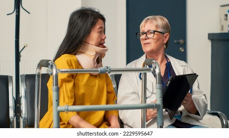 Physician using digital tablet to consult patient with cervical neck brace, sitting in waiting area lobby. Attending medical appointment with doctor, recovering after fracture accident. - Powered by Shutterstock