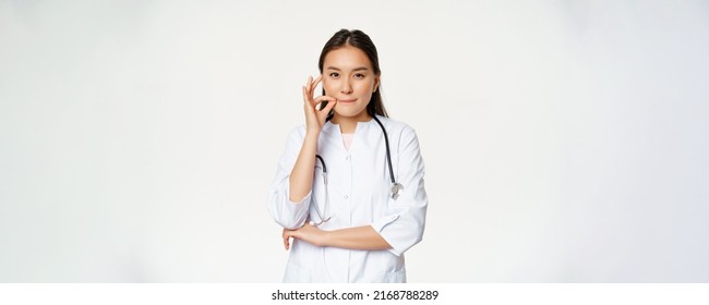 Physician-patient Privilege, Medical Confidentiality. Asian Woman Doctor Showing Silence, Mouth Zip Gesture, Secret, Standing Over White Background