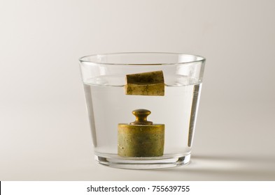 Physics. A cork floats in water and  a antique weight sinks. Archimedes Principle. - Shutterstock ID 755639755
