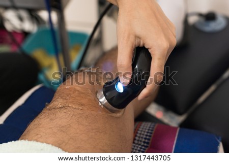 Physiologist using electro stimulation for treat knee pain.Doctor treatment for patient knee and leg muscles injuries, strains and tension in hospital physiotherapy medical rehabilitation clinic.