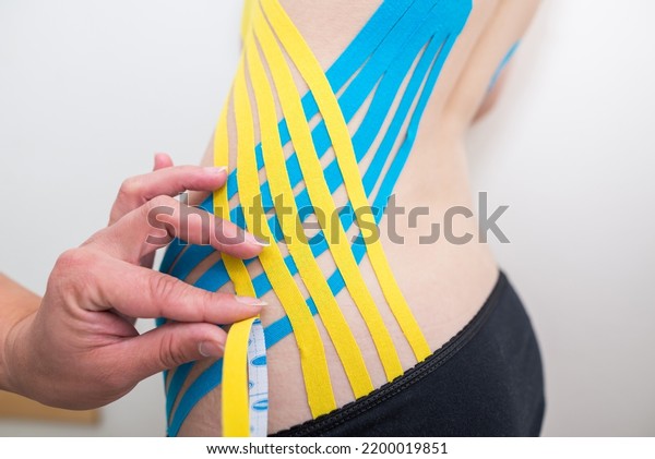 physiotherapist\
applying adhesive elastic therapeutic tape to the side of the\
abdomen of a young adult athletic woman in a doctor\'s office.\
Injury Rehabilitation and\
Healthcare