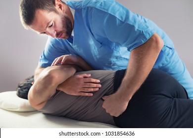 Physiotherapist Doing Healing Treatment On Man's Back. Therapist Wearing Blue Uniform. Osteopathy. Chiropractic Adjustment, Patient Lying On Massage Table