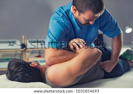 Physiotherapist doing healing treatment on man's back. Therapist wearing blue uniform. Osteopathy. Chiropractic adjustment, patient lying on massage table
