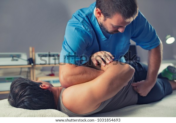 Physiotherapist doing healing treatment on\
man\'s back. Therapist wearing blue uniform. Osteopathy.\
Chiropractic adjustment, patient lying on massage\
table