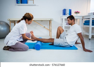 Physiotherapist Doing Leg Therapy To A Man Using Foam Roll In Clinic