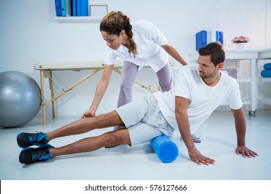 Physiotherapist Doing Leg Therapy To A Man Using Foam Roll In Clinic