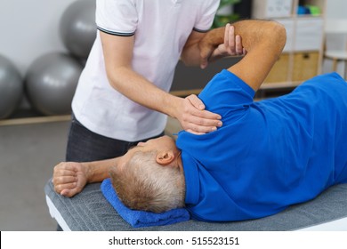 Physiotherapist doing shoulder exercises with an elderly male patient to increase his mobility and restore functionality