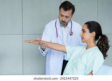 physiotherapist examines the extended arm of a female patient, focusing on her physical therapy. Intense concentration is shown by a therapist assessing a patient's arm mobility in a medical setting. - Powered by Shutterstock