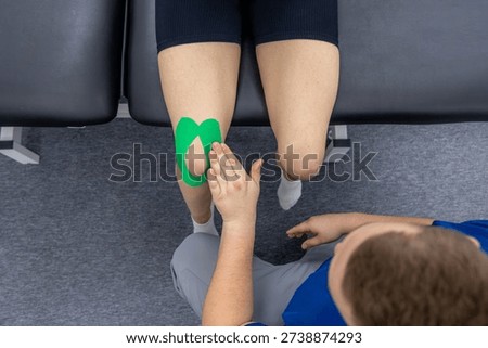 A physiotherapist explains next steps while the female patient sits on a treatment table with green knee tape. Plenty of copy space, neutral tones, and a personalized rehab care feeling.