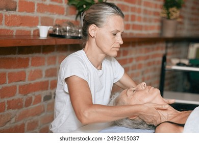 Physiotherapist gently manipulating the neck of a senior woman lying on a massage table in a clinic - Powered by Shutterstock