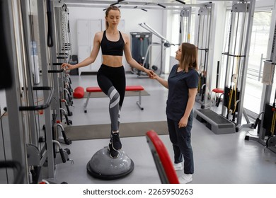 Physiotherapist helping female patient with rehabilitation. Balance exercise with bosu ball. Woman and doctor during rehab physiotherapy in gym - Powered by Shutterstock