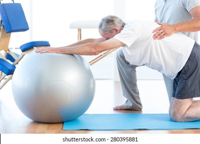 Physiotherapist Helping Man With Exercise Ball In Medical Office