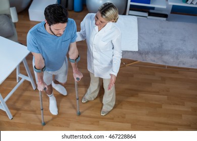 Physiotherapist Helping Patient To Walk With Crutches In Clinic