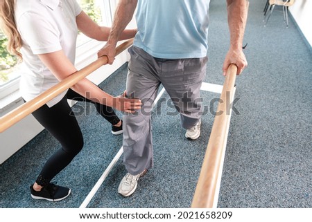 Physiotherapist helping senior man in rehabilitation walking on the bars