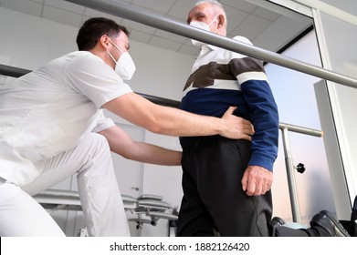 Physiotherapist Helping Senior Patient Walk Between Parallel Bars. 