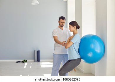 Physiotherapist helping young woman do wall squats with fit ball to get rid of backache and regain spinal health. Young female patient doing back exercise using fitball in physio room of modern clinic - Powered by Shutterstock