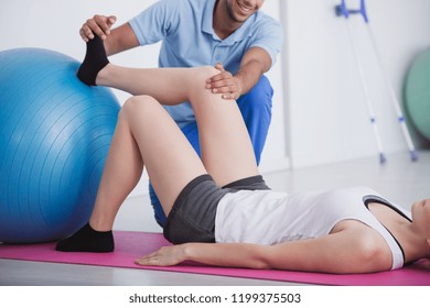 Physiotherapist Holding Knee And Foot Of His Patient During Rehabilitation With A Ball