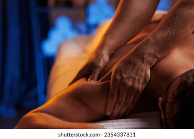 Physiotherapist massaging male patient with damaged shoulder muscle, treating sports injuries. Relaxing professional shoulder massage in cozy atmosphere, reboot on the weekend, end of difficult week. - Powered by Shutterstock