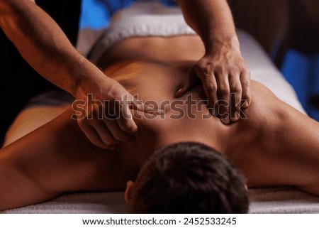 Physiotherapist massaging male patient with damaged shoulder muscle, treating sports injuries. Relaxing professional shoulder massage in cozy atmosphere, reboot on the weekend, end of difficult week.