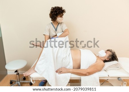 Physiotherapist performing leg massage to mature woman with towels