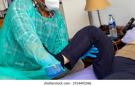 Physiotherapist Performing Rehabilitation Exercises. Unrecognizable Physiotherapist Covered With A Mask, Sanitary Gown And Protective Gloves, Performs Rehabilitation Exercises On A Paraplegic Woman.