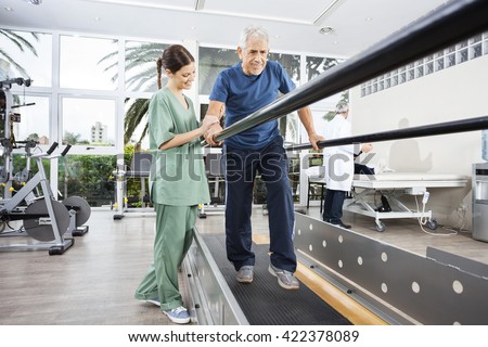 Physiotherapist Standing By Smiling Patient Walking Between Para