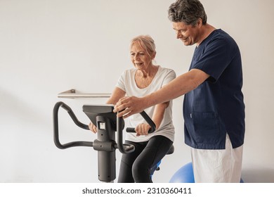 Physiotherapist working with an elderly female patient, rehabilitation practice on exercise bikes and cardio-vascular strengthening, copy space - Powered by Shutterstock