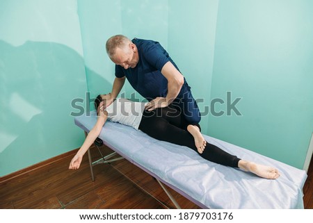 A physiotherapist working with an patient doing mobility and functional exercises with his knee as he lies on the couch for examination