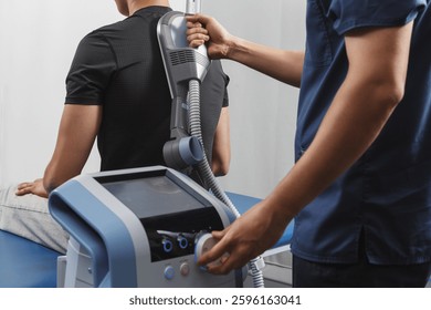 Physiotherapy session with electromagnetic therapy device applied to patient's back. Modern rehabilitation treatment for pain relief and muscle recovery in a medical clinic. Close-up view.