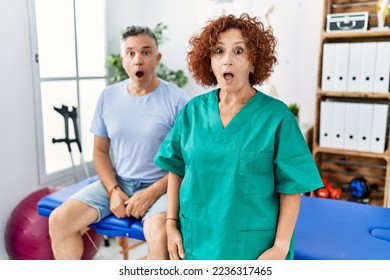 Physiotherapy woman working at pain recovery clinic with patient scared and amazed with open mouth for surprise, disbelief face 