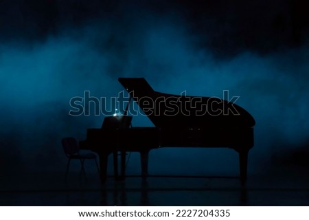 Piano in dramatic ambiance in concert hall, deep color. Silhouette pianon the empty scene