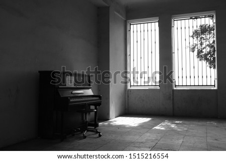 Piano in an empty room, there are bars in the windows. In black and white.