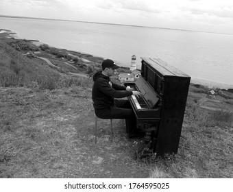 Piano in a field by the sea. Piano in the open. In the background is a lighthouse. The guy is a musician.
