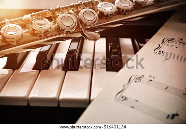 Piano and flute with golden shine\
and sheet music. Horizontal Composition.Front\
view