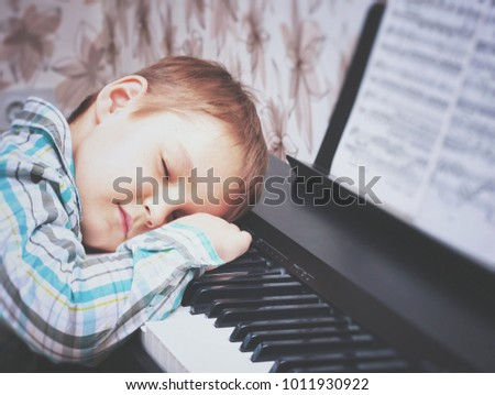 Piano keys. The boy is sleeping on the piano keys. Hands of the boy on the piano keys. The boy is tired and asleep after piano lessons.