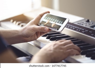 Piano lesson online. Man watching video tutorial with mobile phone and practising playing. Person learning to play an instrument with an internet course and class. Pianist training with smartphone.